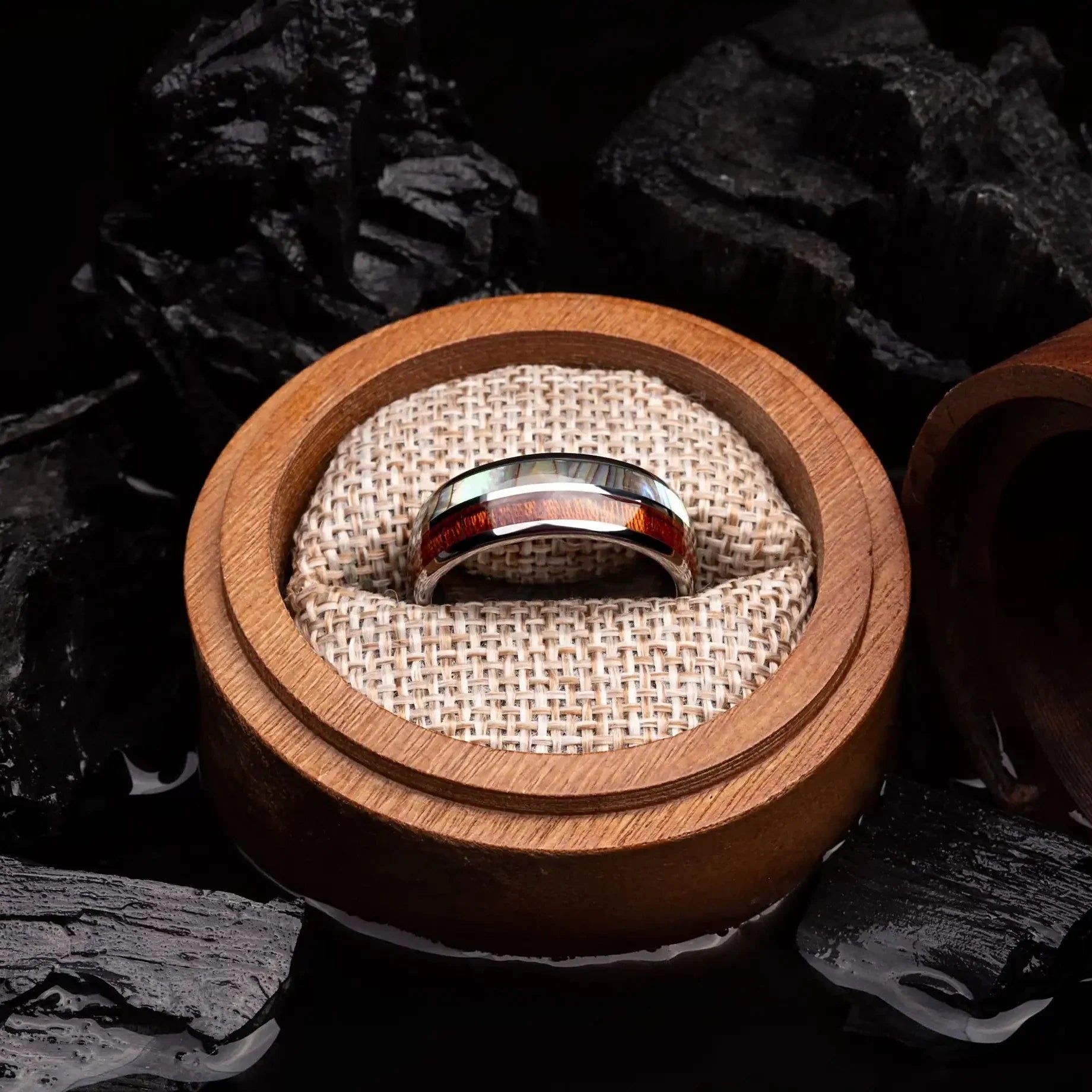 Brushed silver tungsten ring with abalone shell and koa wood. The ring is placed inside a round wooden box.